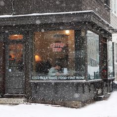 a cold winter day with snow falling on the ground and people sitting at tables in front of a coffee shop