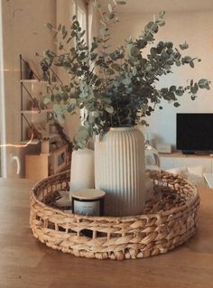 a wicker basket with vases and greenery in it on a wooden table