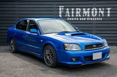 a blue subarunt parked in front of a garage door with the words fairmont sports and classics written on it