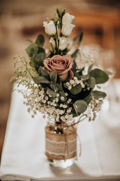 a vase filled with flowers and greenery sitting on top of a white table cloth