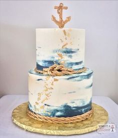 a white and blue cake with an anchor on top is sitting on a gold platter