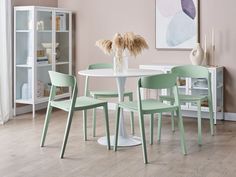 a white table with four mint green chairs and a vase full of flowers on it