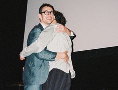 two people hugging each other in front of a projector screen