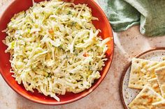 a red bowl filled with coleslaw next to crackers on a white table