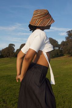 a woman wearing a hat and dress walking in the grass with her back to the camera