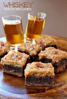 some brownies are sitting on a wooden plate with two glasses of beer in the background