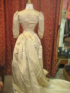 "1880's, 34\" bust, ecru silk faille, bustled and trained skirted wedding gown. A 19th century take on an 18th century lace up, low cut bodice. Bodice has a sharply pointed bottom, below waist, and 3/4 length cuffed sleeves. The bodice curves over hips, and is shorter in back than front. Bustled skirt has steel covered hoops built into back of skirt , and elaborate drapery forming into a long long train. Skirt has scalloped edge at bottom of the front, the bottom of train has a covered dust ruff Fitted Victorian Dress For Debutante Ball, Historical Ball Gown Wedding Dress, Wedding Victorian Dress With Boned Bodice, Victorian Style Crinoline Ball Gown Dress, Vintage Victorian Dress For Debutante Ball, Vintage Victorian Ball Gown With Boned Bodice, Fitted Cream Victorian Ball Gown, Victorian Ball Gown For Debutante Ball, Marie Antoinette Style Victorian Wedding Ball Gown