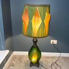 a green lamp sitting on top of a carpeted floor next to a blue wall