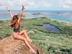 a woman sitting on top of a rock with her arms in the air