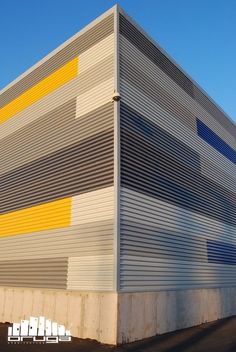 an industrial building with yellow and grey stripes on it's side, against a blue sky