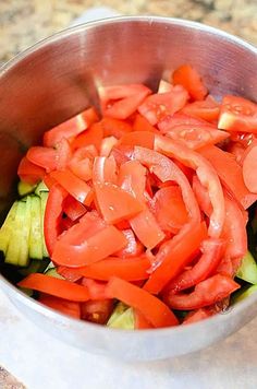 a metal bowl filled with sliced tomatoes and cucumbers