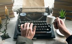 a person typing on an old fashioned typewriter next to a candle and some books