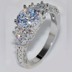 a white gold engagement ring with three stones on the band and an oval center stone surrounded by smaller round brilliant cut diamonds