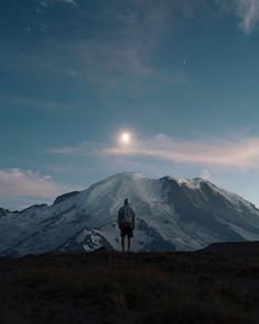 a man standing on top of a mountain under a moon filled sky with mountains in the background