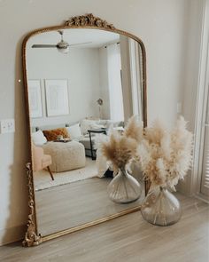 a mirror sitting on top of a wooden floor next to a vase filled with flowers