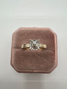 an engagement ring with a princess cut diamond in a velvet box on top of a white wall