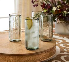 three glass vases filled with water and lemon slices on a wooden table next to flowers