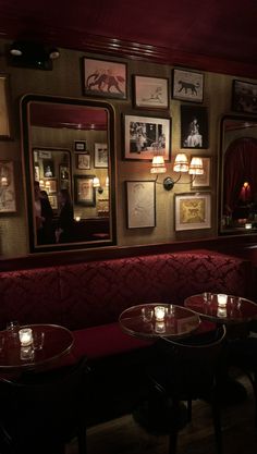 a dimly lit restaurant with red booths and framed pictures on the wall above them, along with candles