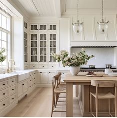 a large kitchen with white cabinets and wooden table in the center, surrounded by stools