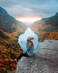 a woman sitting on top of a cliff overlooking a river