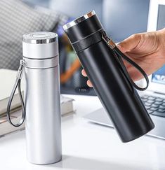 a person holding a black and silver flask next to a laptop