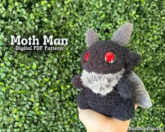 a hand holding a small stuffed animal in front of green bushes with the words moth man on it