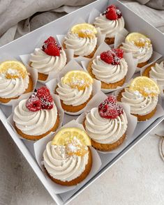 cupcakes with white frosting and raspberries in a box on a table