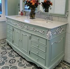 a bathroom vanity with two sinks and flowers in a vase on the sink counter top