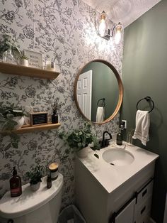 a bathroom with green walls and floral wallpaper on the walls, along with a round mirror