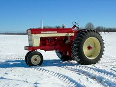 a red and white tractor parked in the middle of a snow covered field on a sunny day