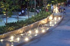 people are walking around in the park at night with water fountains and lights on them