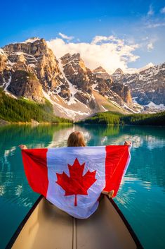 a person sitting in a canoe with a canadian flag on their lap and mountains in the background