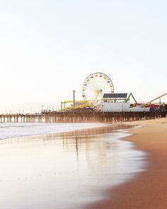 a ferris wheel sitting on top of a sandy beach next to the ocean and pier