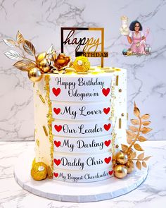 a birthday cake decorated with gold and red decorations on a marble table top next to a happy birthday card