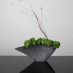 a black vase with some green plants in it