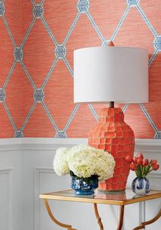 an orange vase with white flowers sits on a table in front of a patterned wallpaper