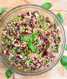 a glass bowl filled with rice and vegetables on top of a wooden table next to green leaves