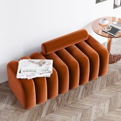 an orange couch sitting on top of a wooden floor next to a table with a cell phone