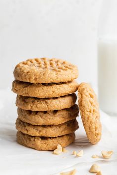 a stack of cookies next to a glass of milk on a white tablecloth with almonds