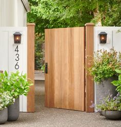 an open wooden door in front of a white house with two planters on either side