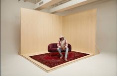 a man sitting on top of a red couch in front of a wooden paneled wall