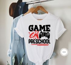 "Game On Preschool Shirt Hi! Welcome to my store, I'm delighted to see you here. My store's main goal is to provide you with premium everyday apparel with the best graphic t-shirts.  DESCRIPTION * Printed and shipped from the USA. * We use state of art printing on soft and quality shirts. * Different size options; crewneck, youth, women's v-neck, toddler, and baby size options.  * Effective customer service and expedited shipping.  * Solid colors are 100% airlume combed and ringspun cotton.  * Heather colors 52/48 cotton/polyester. * Shoulder taping. Side-seamed. Fitted at bicep. Tear-away label. 4.2 oz. SIZES AND COLORS * Please refer to the size charts for measurements before placing an order. * You can compare our numbers to one of your favorite shirts to make sure. * Unisex shirts are School T-shirt With Heat Transfer Vinyl, Cotton T-shirt With Heat Transfer Vinyl For School, Game Day Cotton T-shirt For End Of School Year, Cotton T-shirt For Game Day, End Of School Year, White Slogan Shirt For School, Gamer Style White Top For Streetwear, White Cotton Gamer T-shirt, Cotton Slogan Shirt For School, Cotton School Shirt With Slogan