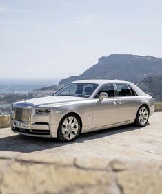 a silver rolls royce parked on top of a stone wall next to the ocean and mountains