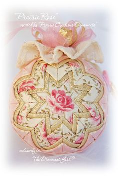 a decorative ornament with pink roses on it's side and ribbon around the top