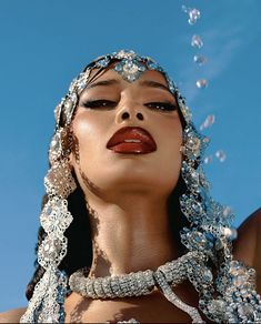 a woman with her face covered in beads and chains, blowing bubbles into the air