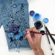 a woman is painting a jean jacket with flowers on it