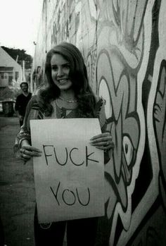 a woman holding a sign in front of graffiti covered walls