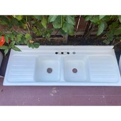 a white sink sitting on top of a tiled floor next to a tree and potted plants