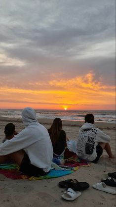 three people sitting on the beach watching the sun set