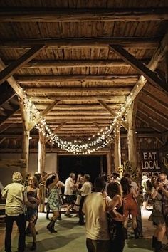 a group of people standing around in a room with lights on the ceiling and wood beams